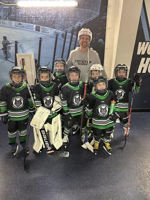 A Mites group poses with their coach in the hallway at LaHaye Ice Center