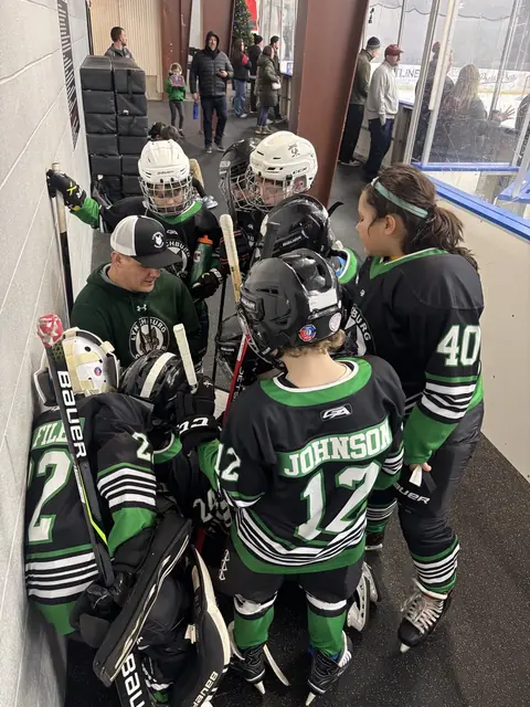 A coach kneels rink-side to talk through the next shift with his players