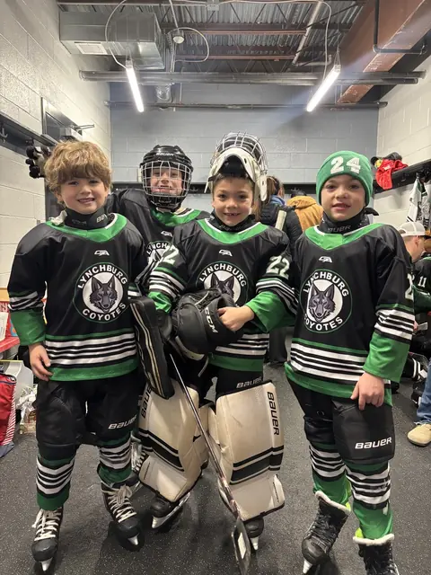 Three teammates and their goalie pose in full gear in the locker room